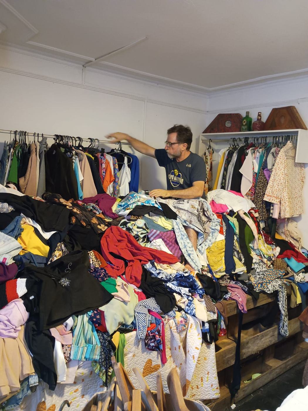 Dono do Atacadista do Brechó separando roupas em cima de uma grande pilha sortida no galpão